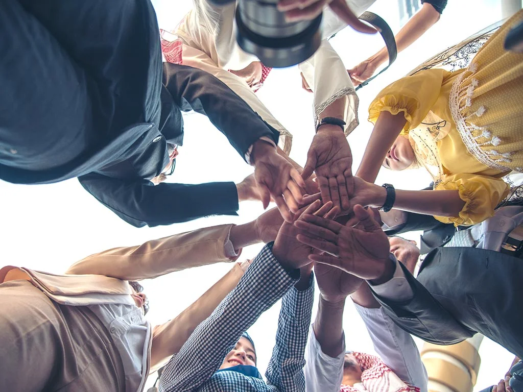 Grupa ludzi łącząca dłonie w środku koła w geście współpracy i integracji, widok od dołu