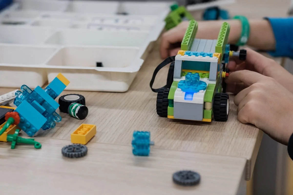 robotyka (2) (Niestandardowy) Zbudowany z klocków LEGO pojazd z silniczkiem i kołami zębatymi na stole podczas warsztatów z robotyki